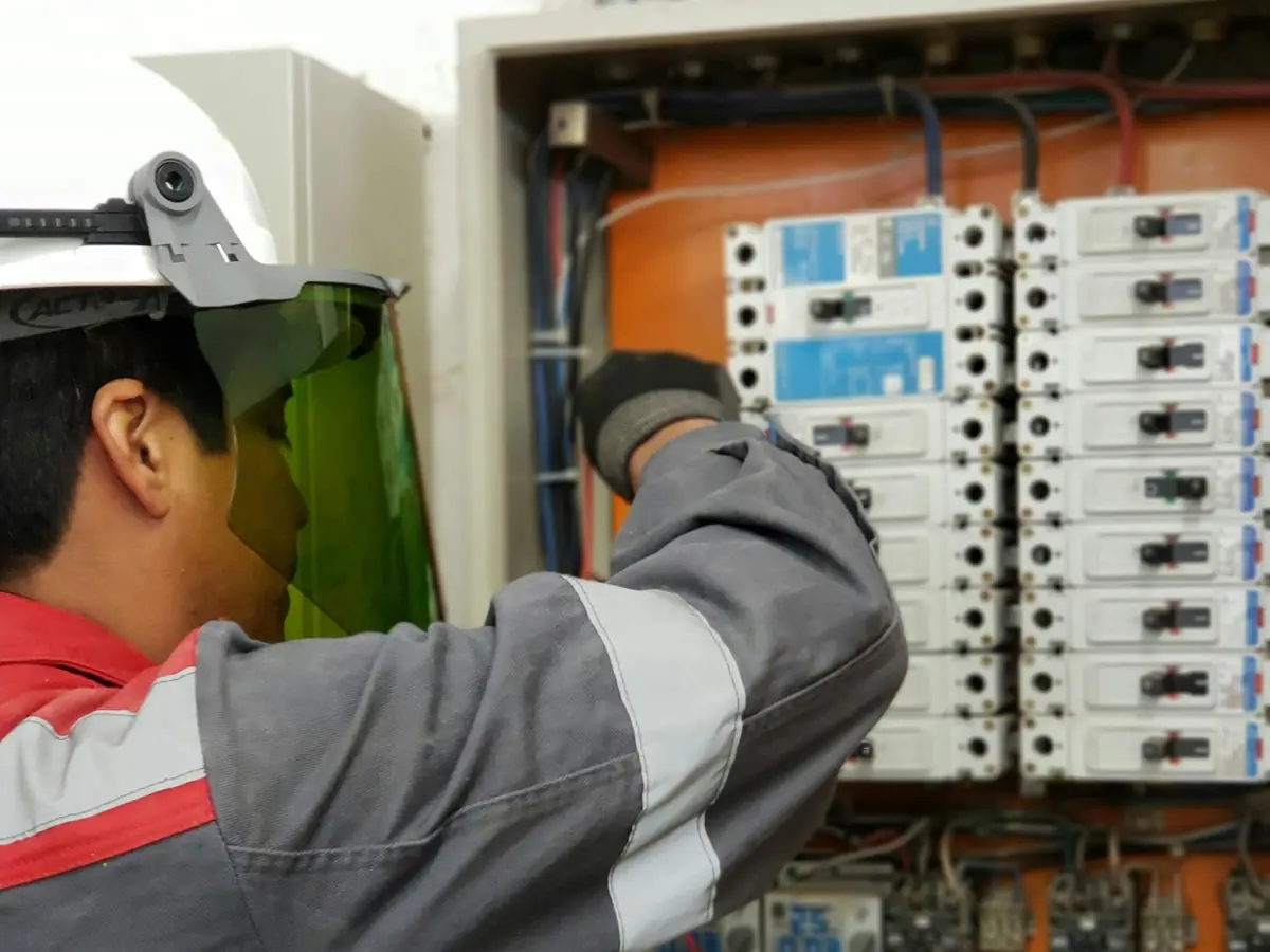 Elektryk w kasku i przyłbicy sprawdza aparaturę w rozdzielnicy