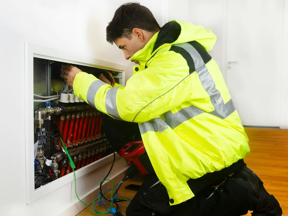 Instalator w kurtce odblaskowej podłącza rozdzielacz instalacji grzewczej